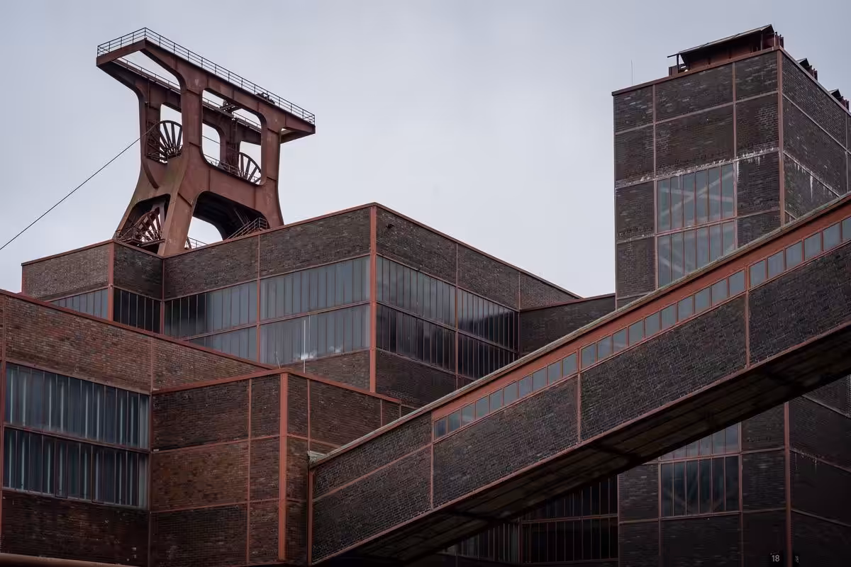 Industrielles Backsteingebäude mit Förderturm vor grauem Himmel.