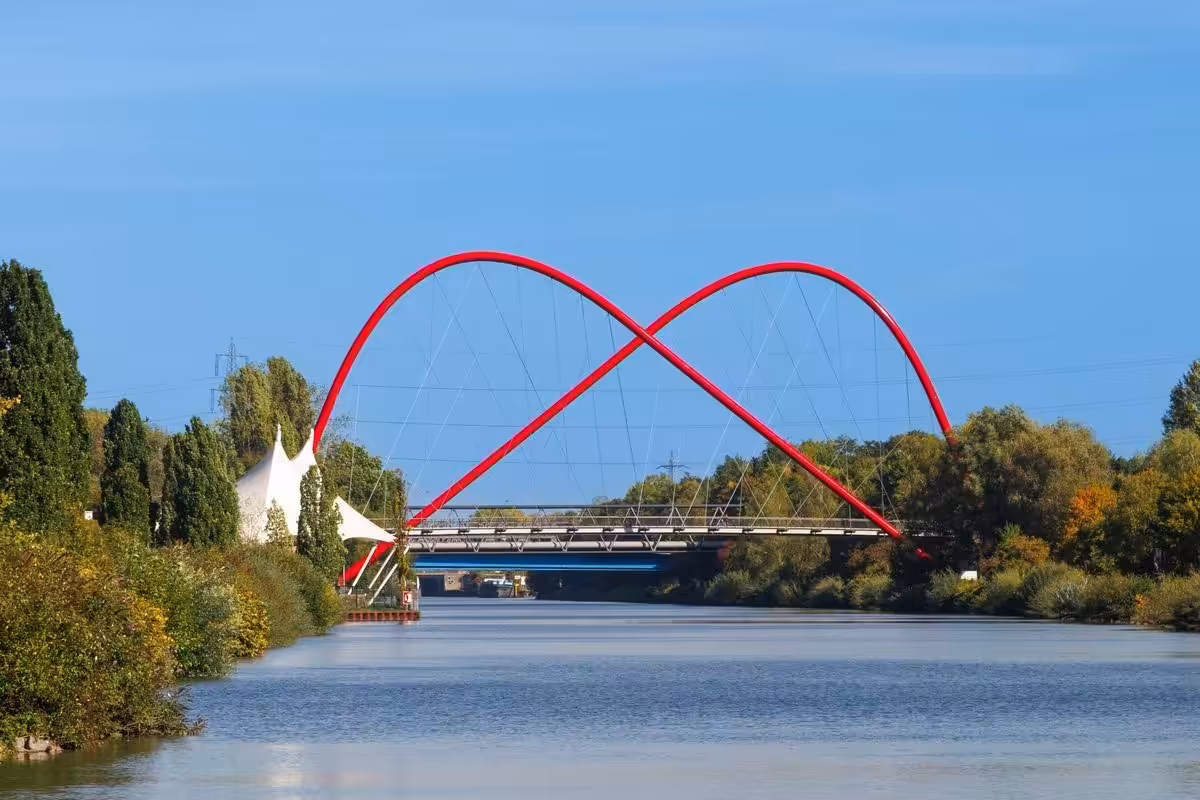 Rote Stahlbrücke über Kanal und Bäume entlang.