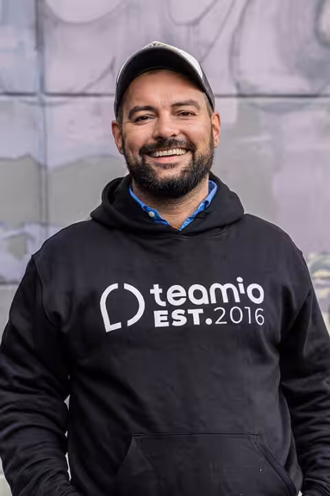 Mann trägt Teamio-Hoodie und Kappe, lächelt.